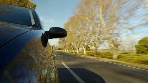 Driving a car, windshield reflection. Hood side reference. Mounted camera, front view. Black car ride. Country road, trees on the side, blue sky, day. Fast Speed / Time-Lapse. HD.
