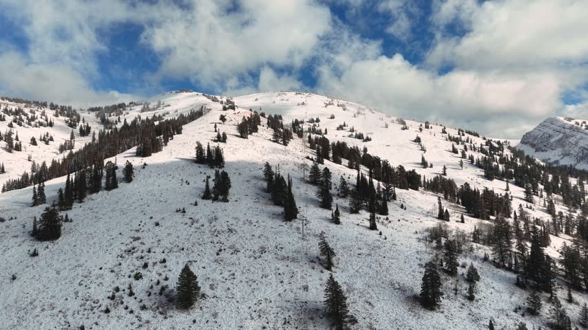 Aerial panorama of snow covered mountain slopes dotted with evergreen trees beneath clouds in Idaho, USA.