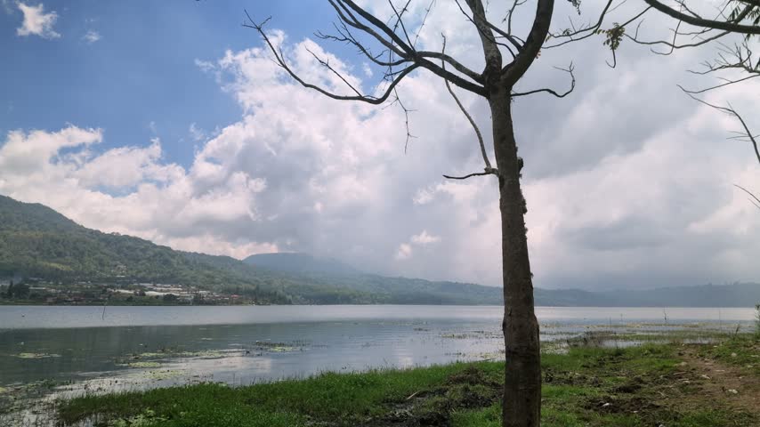 Scenic View of Lake and Mountain Hills Under Cloudy Sky with Tree Silhouette