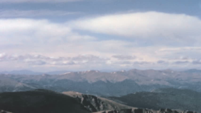 Rocky Mountains landscape in Colorado features rugged foreground ridges above the tree line. Panning view reveals layered distant peaks and scattered snow patches under wispy clouds archival footage.