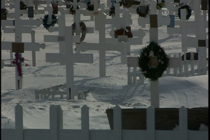 Tilt up from snow to lots of little white wooden crosses with frozen bay in background in Greenland.