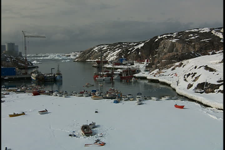 Slow pan across frozen harbor, many boats lay tilted on snowy surface of ice in Greenland.