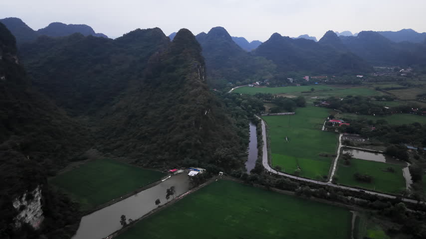 An aerial camera glides past limestone mountains a road and rice fields in Tam Coc Vietnam revealing homes and farms across the valley in daylight.