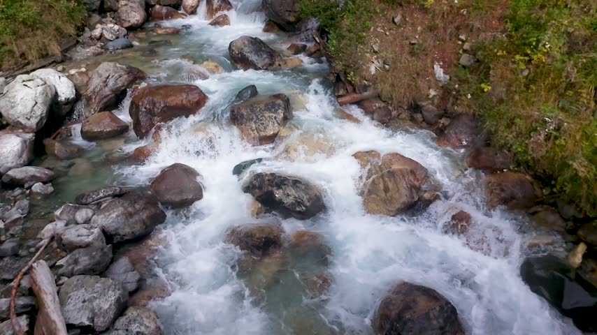 Fast-flowing mountain stream cascading over large rocks and boulders in a natural wilderness setting