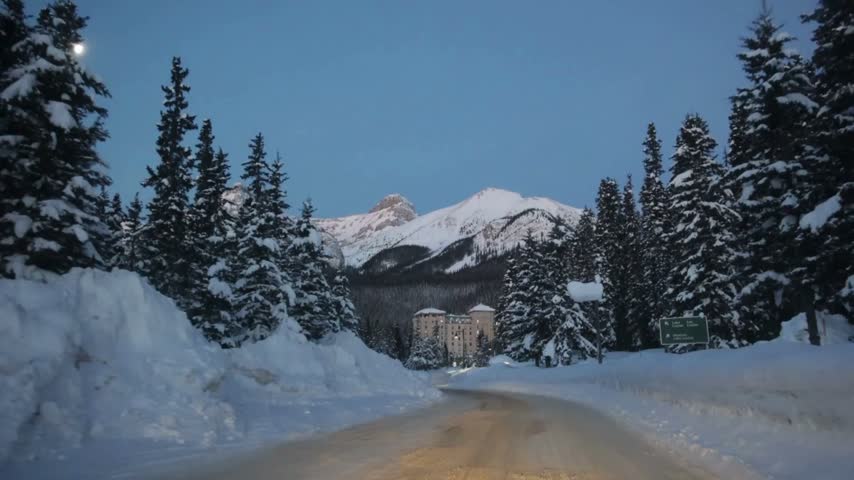 Car traveling forward on snowy mountain highway during winter season surrounded by pine trees and frozen landscape
