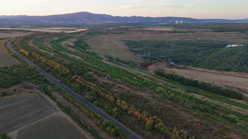 Aerial view of lignite surface mining near Halmajugra, Hungary, with machinery, haul roads, vegetated mine land, farmland and the Mátra Mountains at sunset.