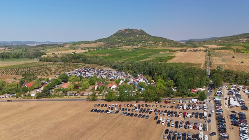 Aerial view of the crowded Sunday market and extensive car parks amid farmland and vineyards in Káptalantóti, Hungary, on a summer day.