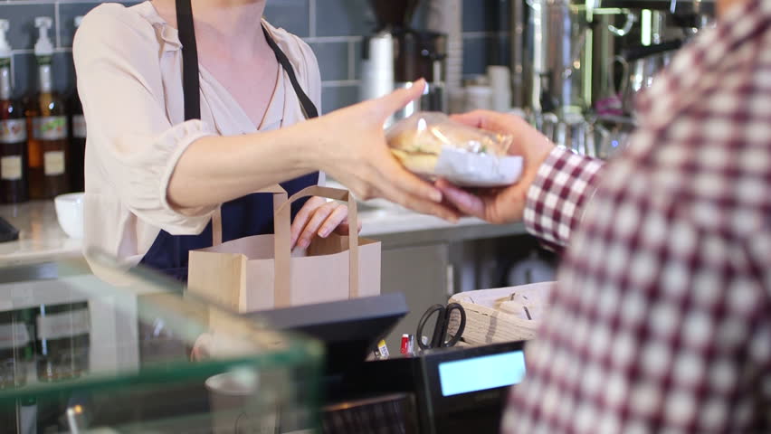 Female seller serving young man sandwich to go