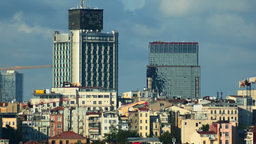 Taksim and Beyoglu urban cityscape showing modern high-rise hotels rising above colorful historic residential buildings under a blue sky. Istanbul, Turkey. Static view