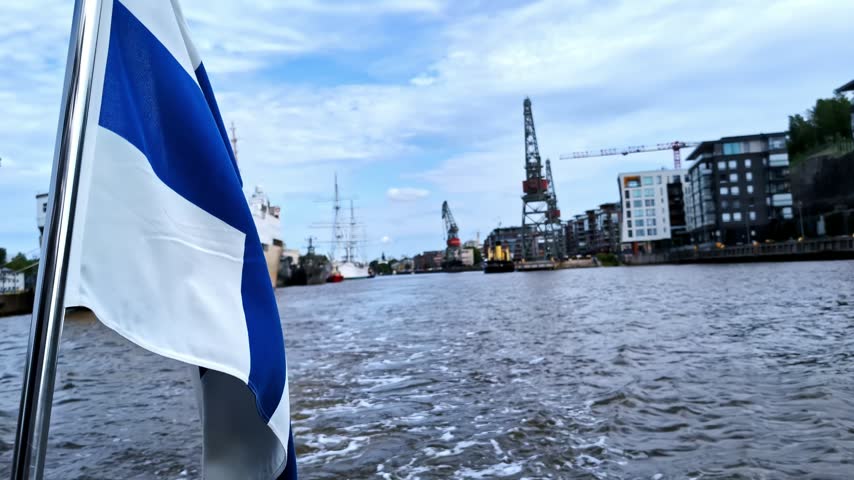 Finnish flag fluttering on moving boat along the Aura River in Turku, Finland