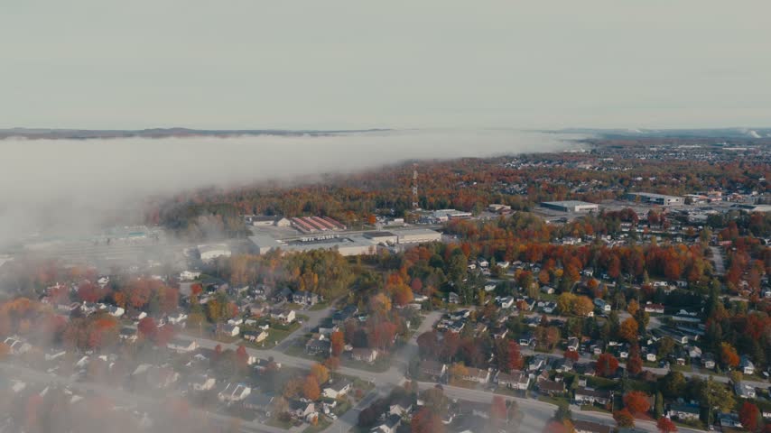 Low Morning Fog Rolls Across A Suburban Town Surrounded By Colorful Autumn Trees And Residential Neighborhoods. - aerial shot