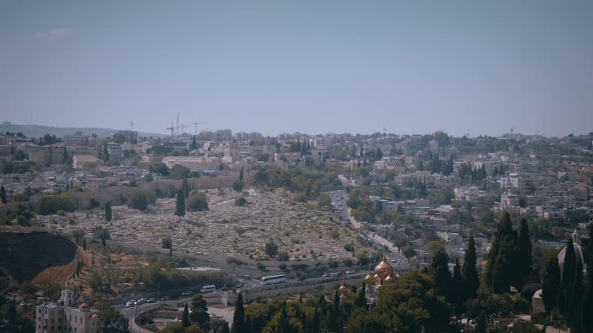 Jerusalem Hillside Cemetery and Cityscape with Golden Church Domes
Low-angle architectural view of Damascus Gate in Jerusalem’s Old City, highlighting its carved pointed arch, decorative stone medallions, narrow arrow slits, and ornate battlements. Bright sunlight illuminates the pale limestone facade, with leafy branches framing the right side against a deep blue sky.