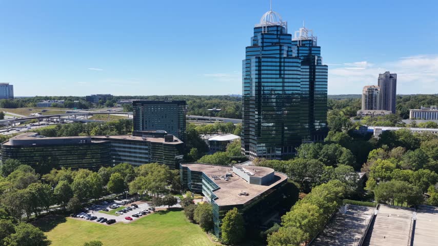 The twin crowned King and Queen towers stand over curved low office buildings, a tree lined parking lot and a sprawling freeway interchange near Perimeter Center, Georgia. Aerial view
