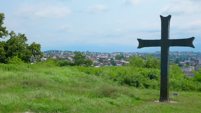 Large stone christian cross standing on a green hill overlooking the city of kutaisi, georgia, a symbol of faith, belief, and orthodox christianity