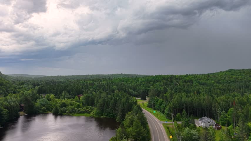 Storm clouds hang over forested hills beside a curving road and lakeshore.