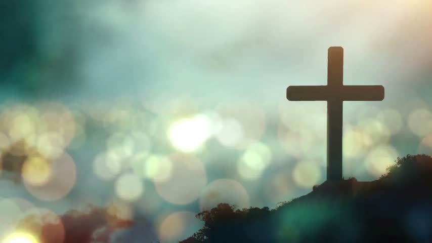 A silhouette of a wooden christian cross on a hill at sunset with bokeh.