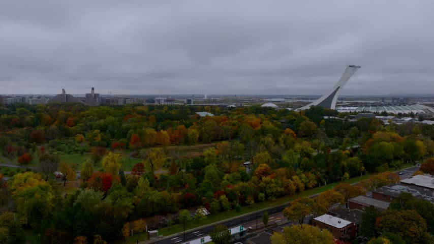 Olympic Stadium, Montreal, Quebec, Canada - Colorful Autumn Foliage Fills a Park With the Iconic Inclined Tower Rising in the Background - Orbit Drone Shot
