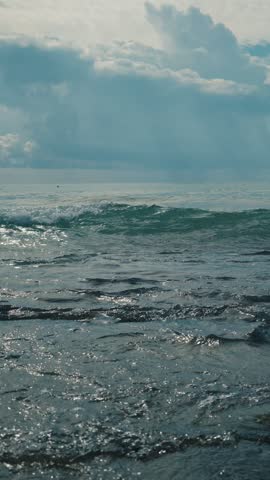 Rolling turquoise wave breaking toward rocky shore under dramatic cloudbank and,