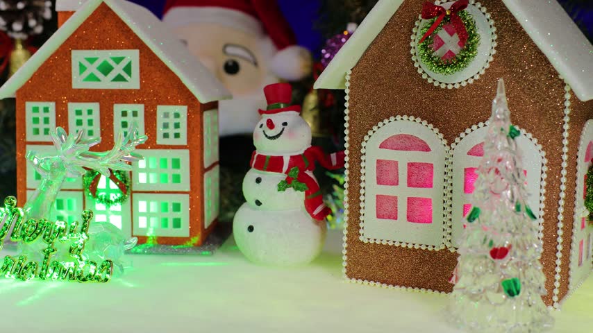 A close-up view in a Christmas village: in front of large, colorful houses complete with Santa Claus and a snowman stands a reindeer with letters