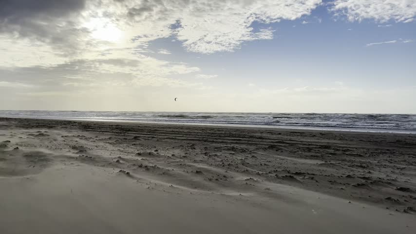 Distant kite surfer riding rough North Sea waves under a stormy cloudy sky, Petten aan Zee, The Netherlands