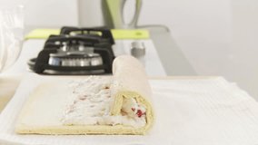 A Swiss roll filled with strawberry cream being rolled up