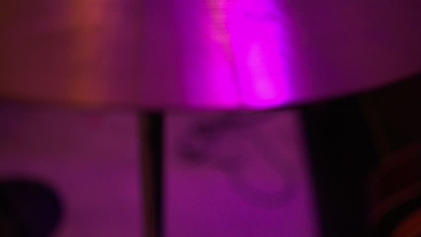 Bronze drum cymbal played with bamboo style percussion rod under atmospheric magenta and purple studio lighting, capturing rhythmic vibrations and instrumental music performance