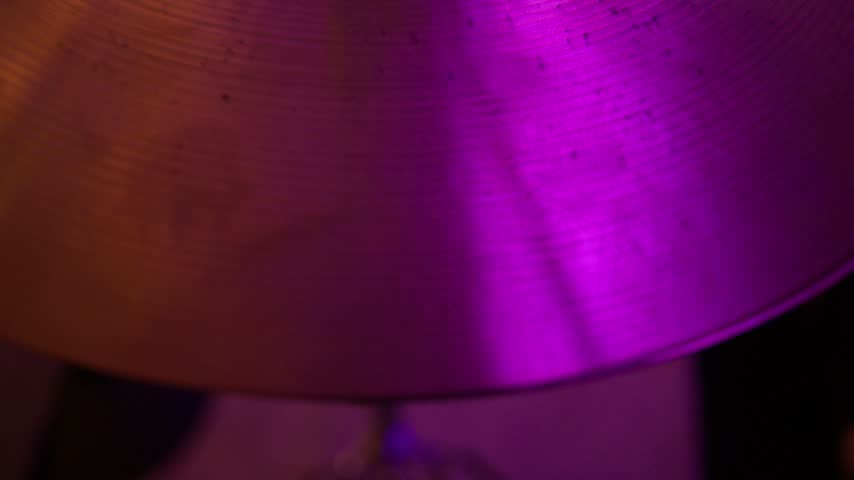 Macro close up of bronze drum cymbal with concentric grooves reflecting pink and purple studio lights, abstract musical instrument texture during professional recording session