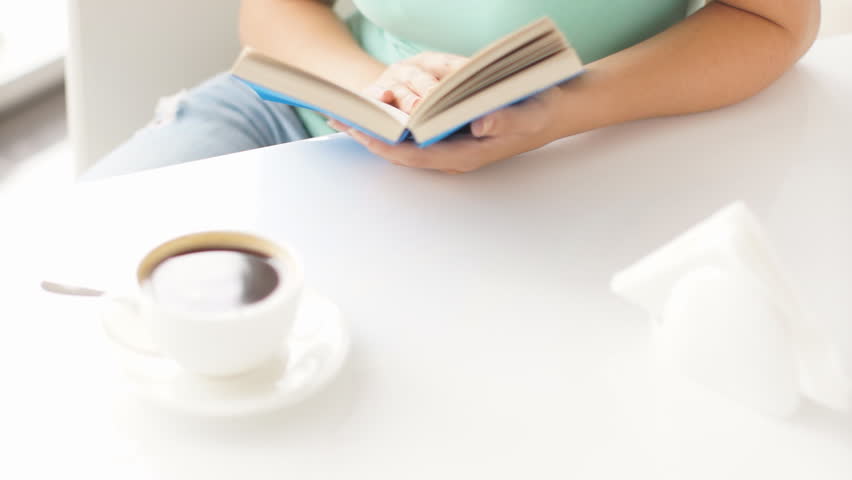 Girl holding blue-covered book  with cup of coffee on foreground
