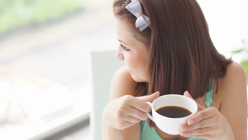 Cute girl holding cup of coffee looking at window and laughing
