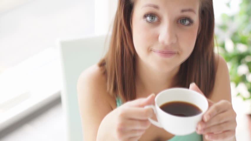 Cute girl holding cup of coffee and smiling at camera
