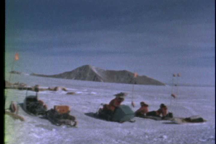 1960s - A group of scientist use snowmobiles and toboggans to reach an area of exposed rock in Antarctica