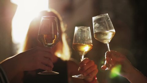 Women holding glasses of white wine making a toast at sunset