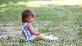 Charming little girl sitting on the lawn and playing with grass
