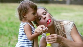 Mother entertaining her baby girl by making iridescent soap bubbles