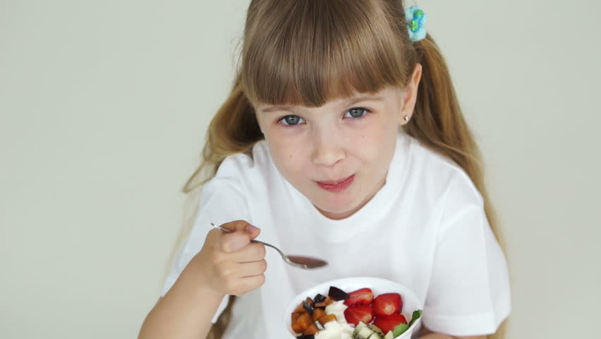 Girl eating yogurt with fruit and smiling
