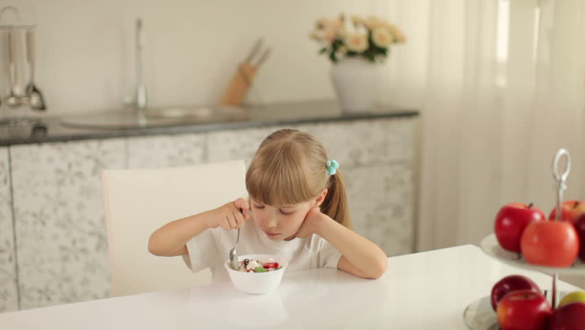Cute little girl sitting in kitchen and eating an ice cream sundae
