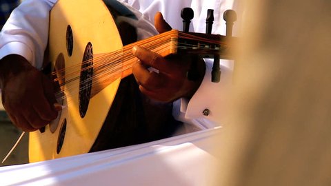 Middle eastern male wearing traditional white robe playing ethnic acoustic oud musical instrument hands only