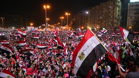 CAIRO, EGYPT - 2013: Protestors wave flags and fireworks go off at a nighttime rally in Cairo, Egypt.