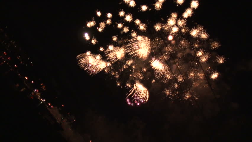 Strong angle on fireworks shooting up in the air and exploding in the night sky.