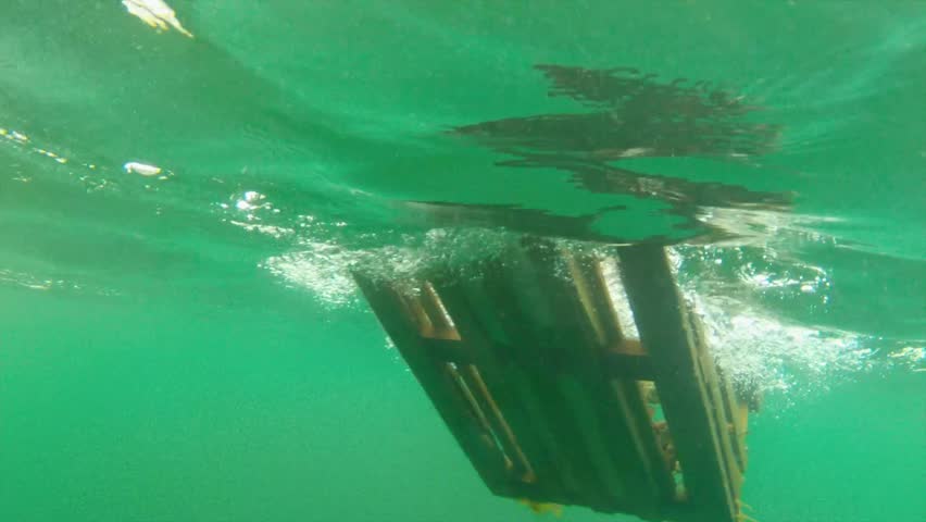 A cool underwater shot of a lobster trap being pulled into a fishing boat from