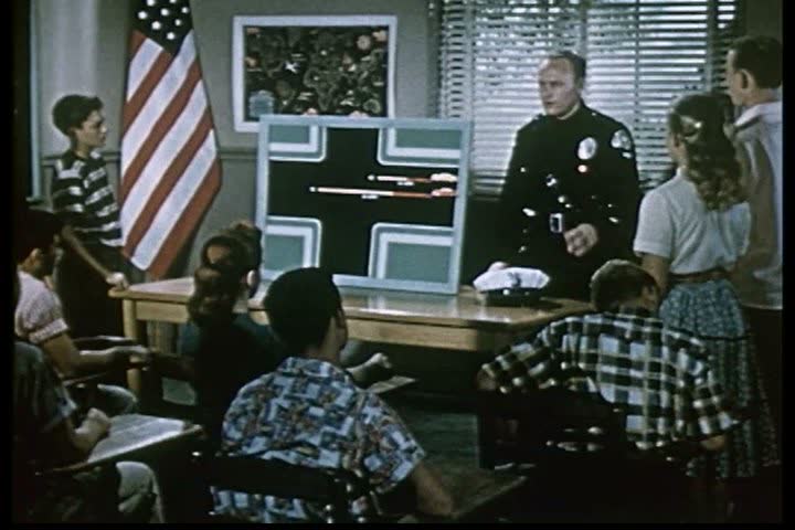 1960s - A police officer lectures a class of young men and women about proper traffic safety during the 1960s