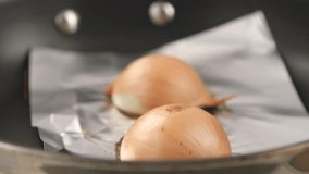 Half an onion being fried in a pan lined with aluminum foil