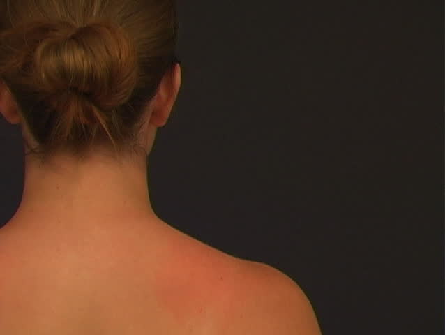 A red circle indicates the area of pain on the right shoulder of an attractive young woman, who then reaches up with her left arm to rub her shoulder muscle.