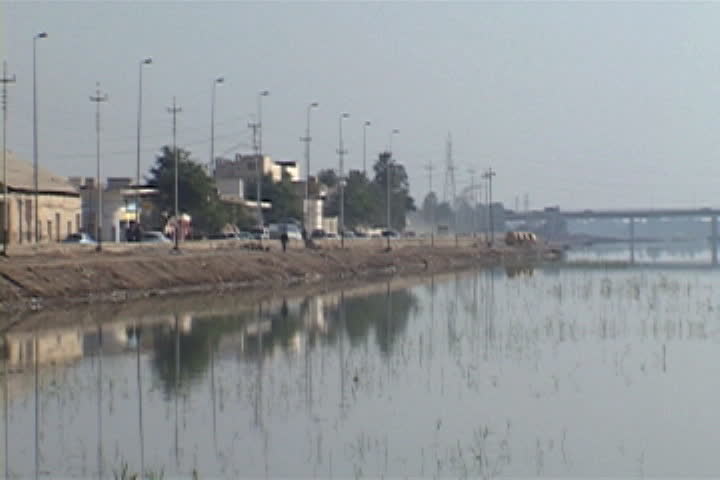 Still water in the Euphrates River, bordered by traffic passing on adjacent road in Nasiriyah, Iraq.