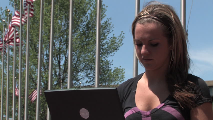 A young woman uses her laptop wirelessly in the park.