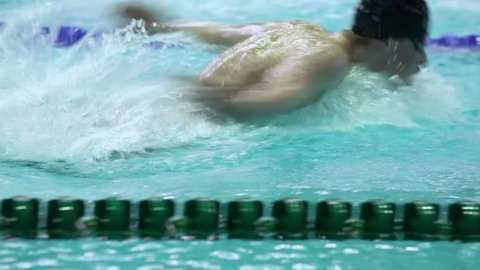 Sportsman swims in butterfly style by track at swimming pool, (unfocused)