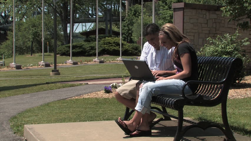 A young couple use their laptop wirelessly in the park.