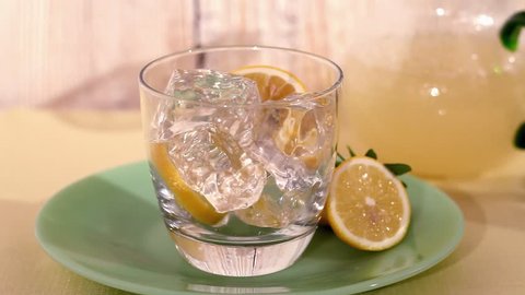 Lemonade being poured into a glass of ice cubes and lemon slices - Βίντεο στοκ