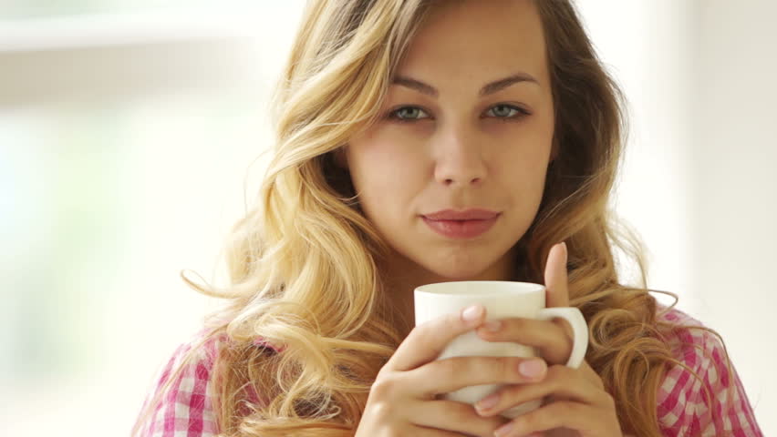 Young woman holding cup of drink and looking at camera with smile
