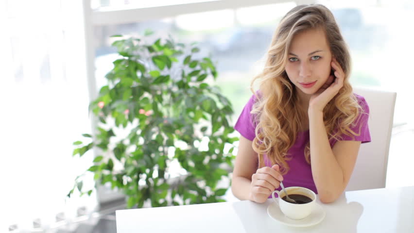 Smiling  young woman sitting at table with cup of coffee and green plant on